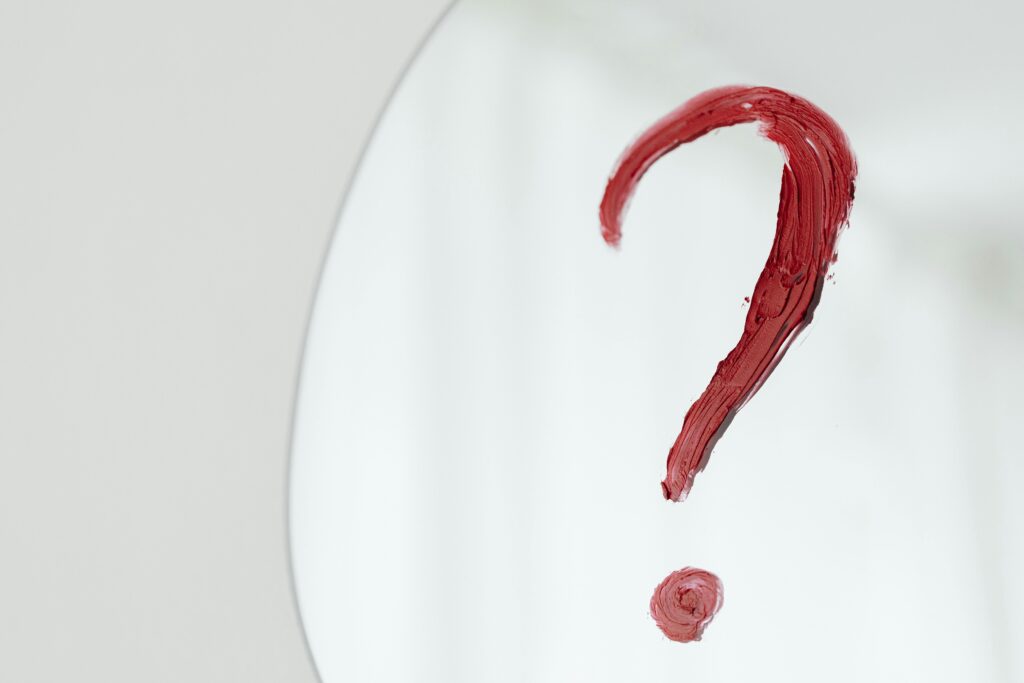 Ponto de interrogação pintado com batom vermelho em um espelho