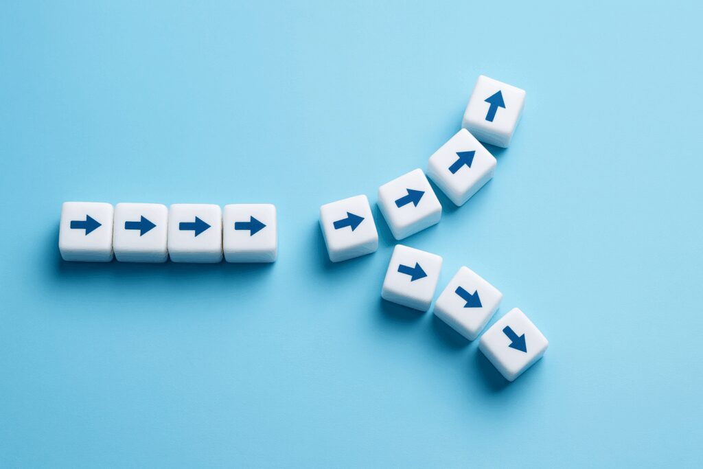 Cubos brancos com setas azuis estão alinhados sobre fundo azul claro, formando um fluxo que se divide em dois caminhos diferentes.