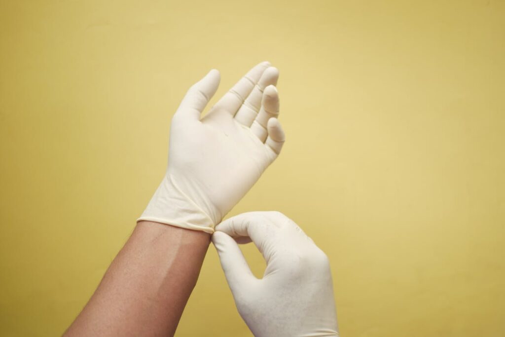 Pessoa vestindo luvas médicas brancas, ajustando uma delas na mão contra um fundo amarelo